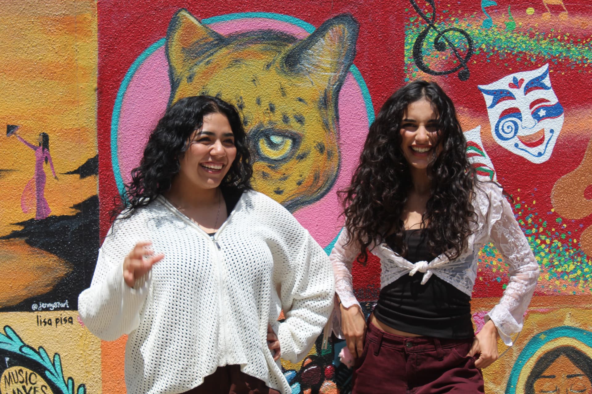 Two vocalists laughing in front of a colorful mural