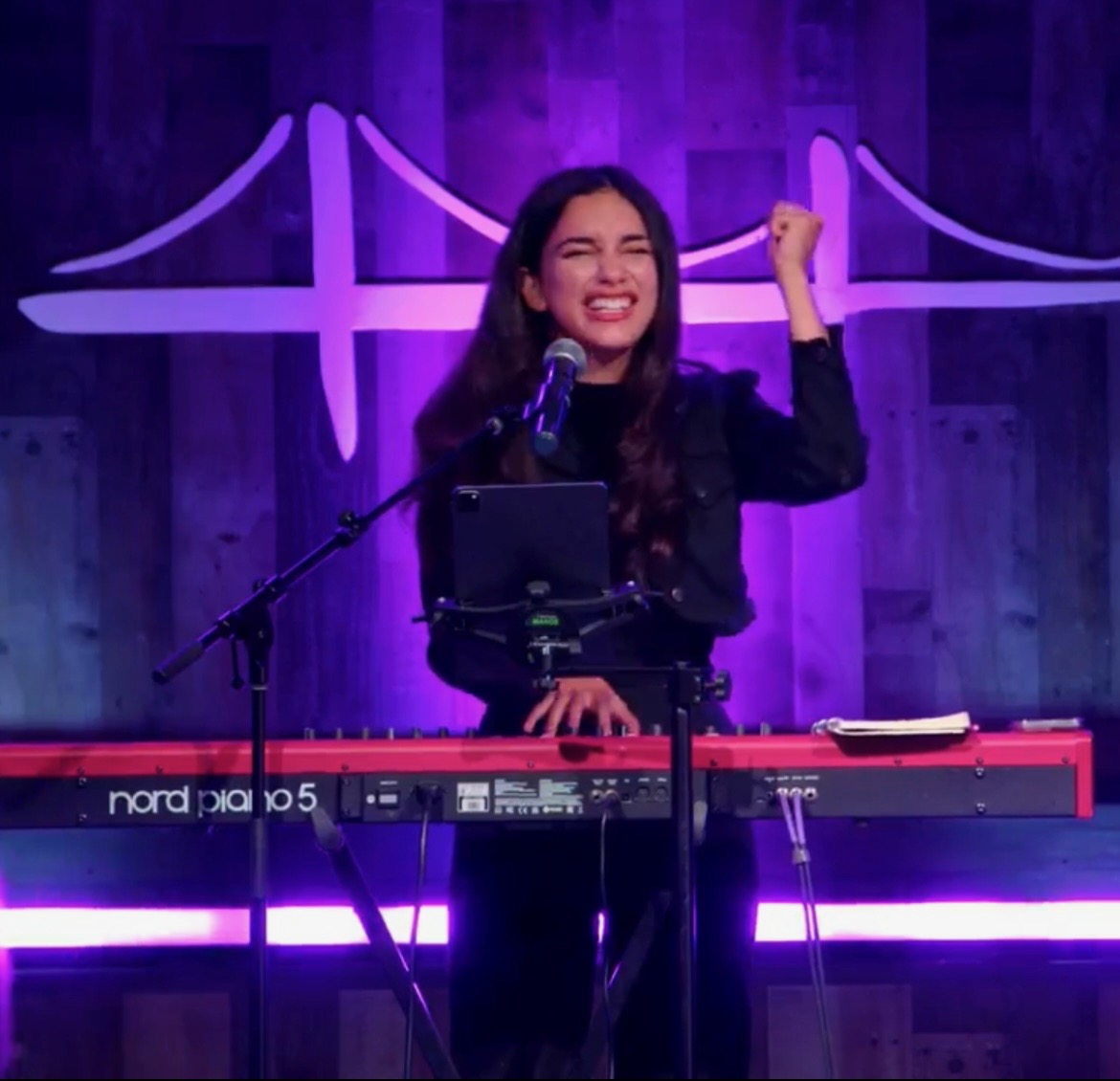 Vocalist performing on stage beneath purple lighting