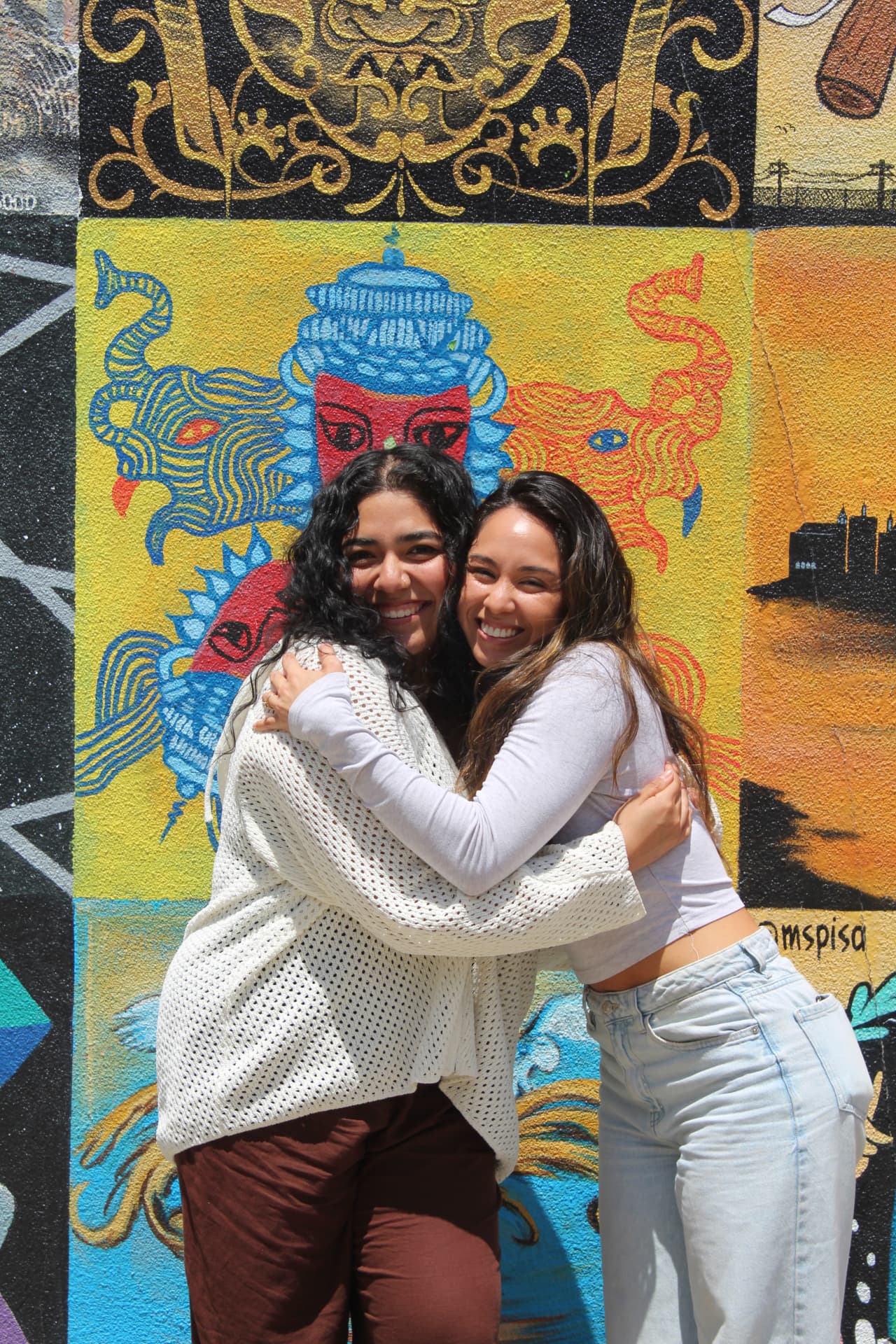 Two members of the collective hugging in front of a mural